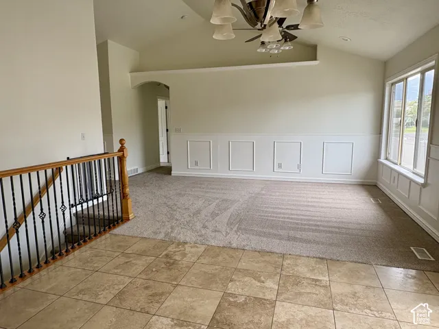 Vaulted ceilings highlight this living space, featuring a decorative ceiling fan with integrated lighting, wainscoting paneling, and a window with an integrated bench