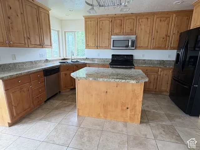 Kitchen featuring light wood cabinetry, stone countertops, a central island, stainless steel microwave, and tile flooring