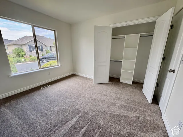 Bright room featuring a large window, neutral carpeting, and a built-in closet with shelving and hanging rods