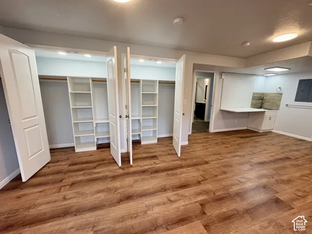 Spacious room featuring wood-finish flooring, two built-in closet systems with shelving and hanging rods, a built-in desk with lower cabinetry, and recessed lighting