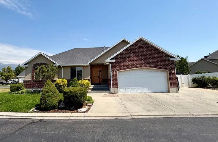 Brick and stucco exterior featuring an attached two-car garage with a white panel door, a concrete driveway, and a front walk leading to the entryway