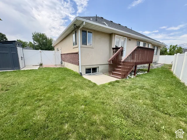 Expansive green space featuring a wooden deck with railing, stucco exterior with brick accent, white vinyl fencing, and a dark grey storage shed