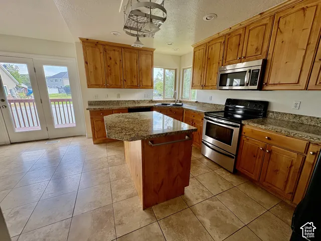 Kitchen featuring wood cabinetry, an island with a countertop, stainless steel appliances, and a tile floor