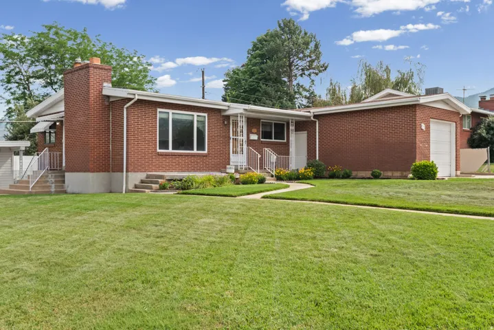 Brick exterior featuring an attached single-car garage, multiple entryways with handrails, and a front lawn with established landscaping