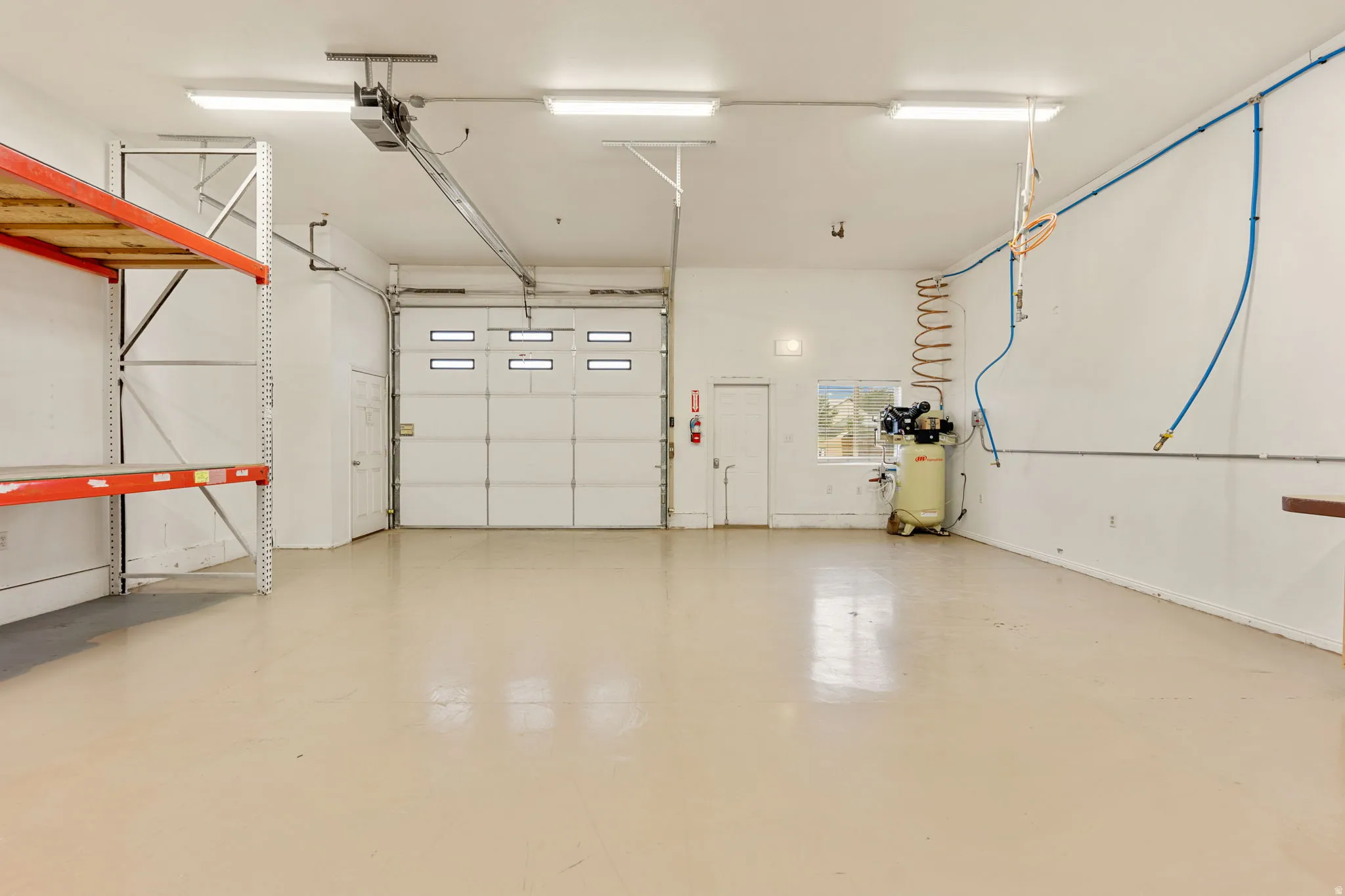 Spacious garage featuring a large overhead door with window inserts, high ceilings, multiple fluorescent light fixtures, and durable epoxy flooring