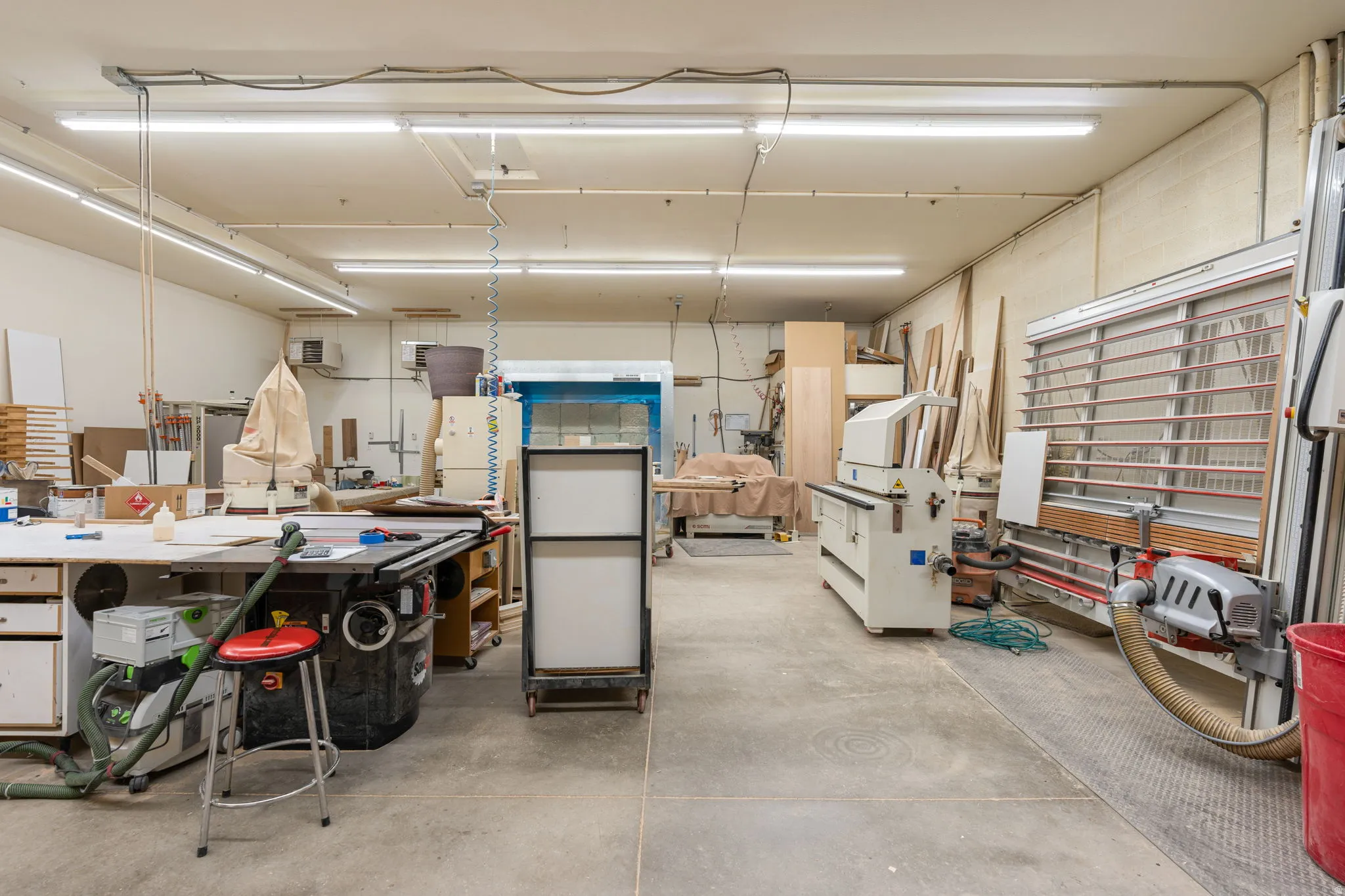 Expansive workshop space with concrete flooring, fluorescent lighting, and extensive built-in work surfaces