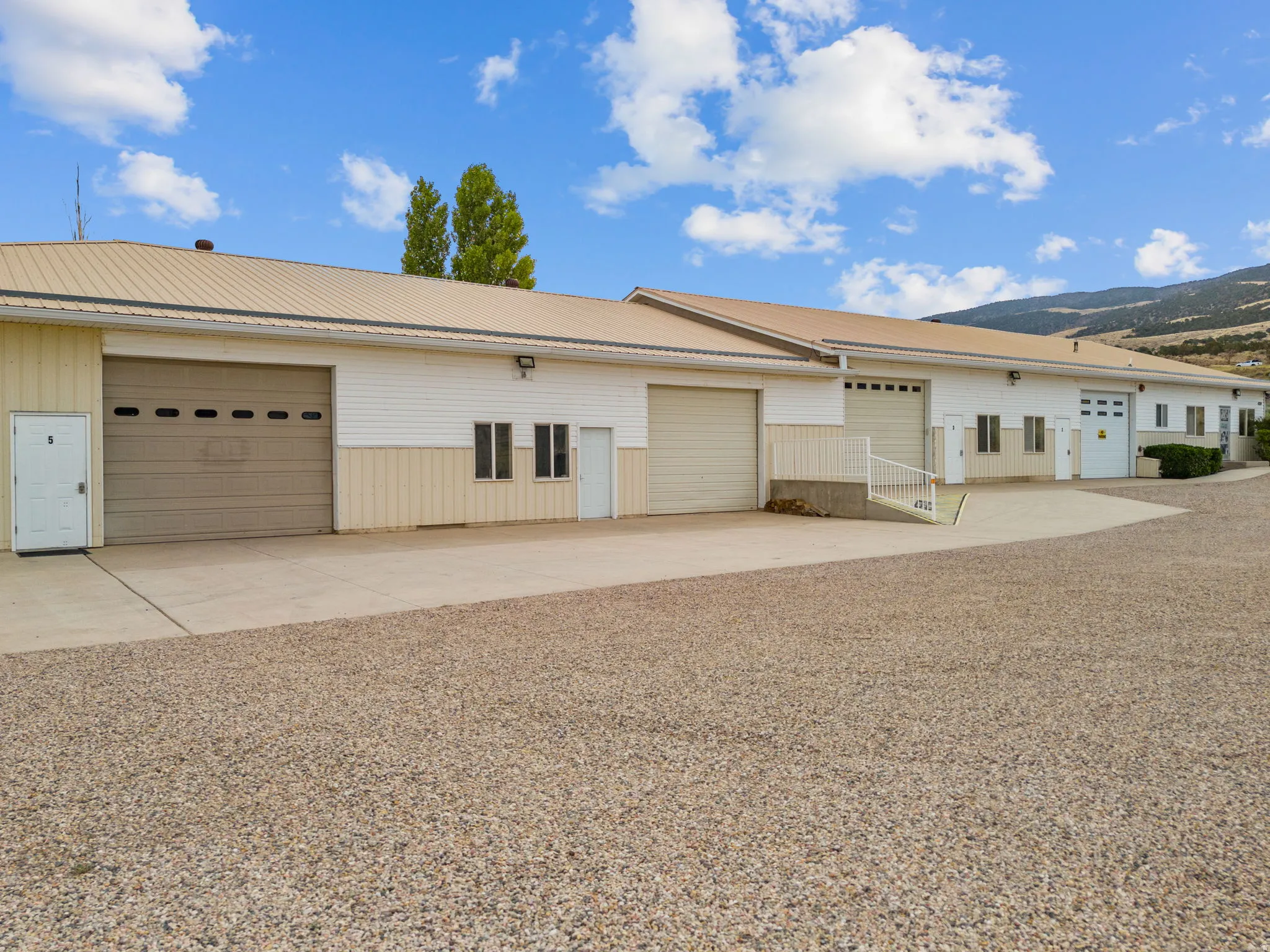 Commercial building featuring multiple garage bays, a metal roof, and a gravel parking area
