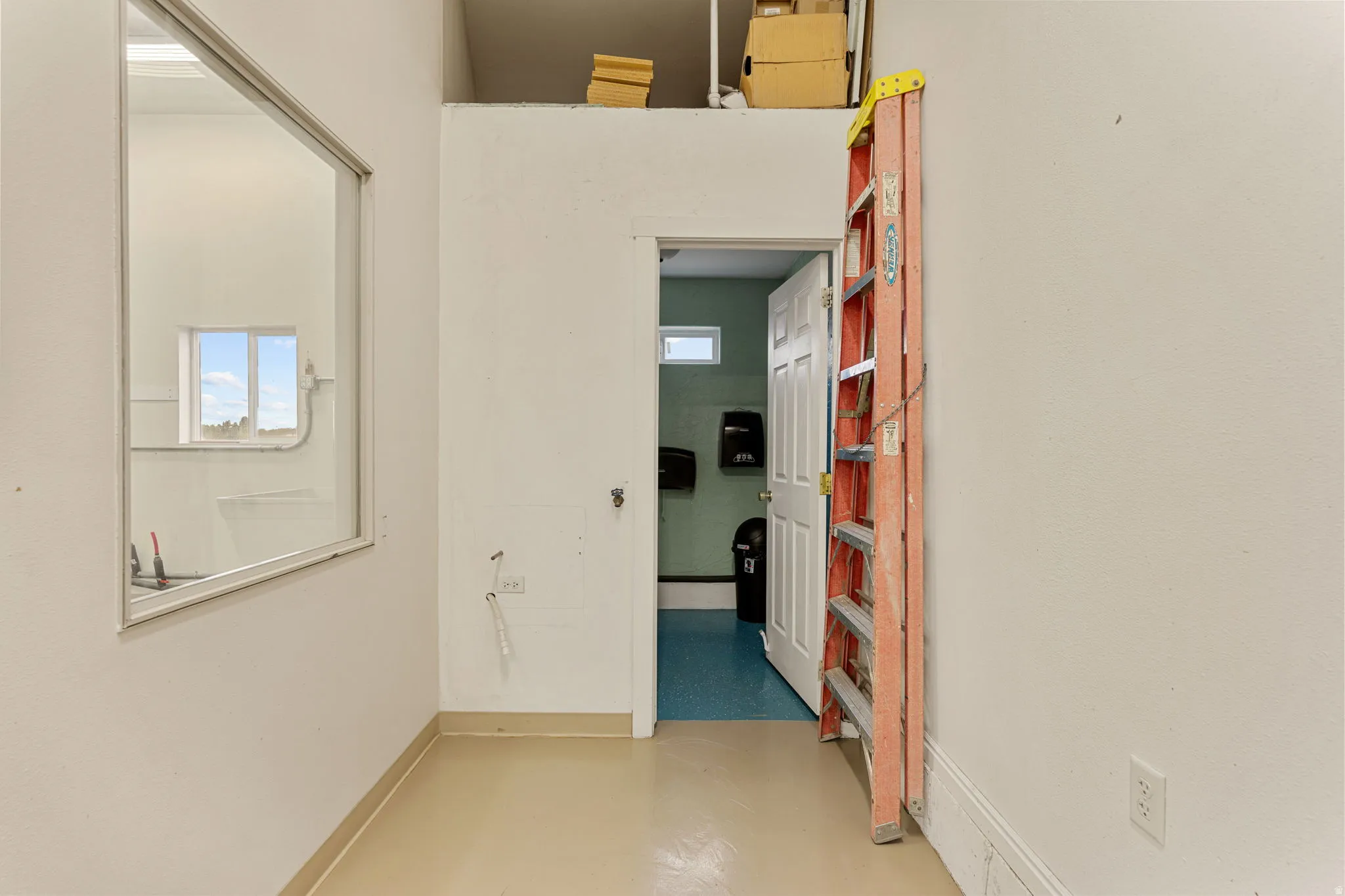 Spacious room with light-toned flooring, high ceilings, and a large interior window providing natural light
