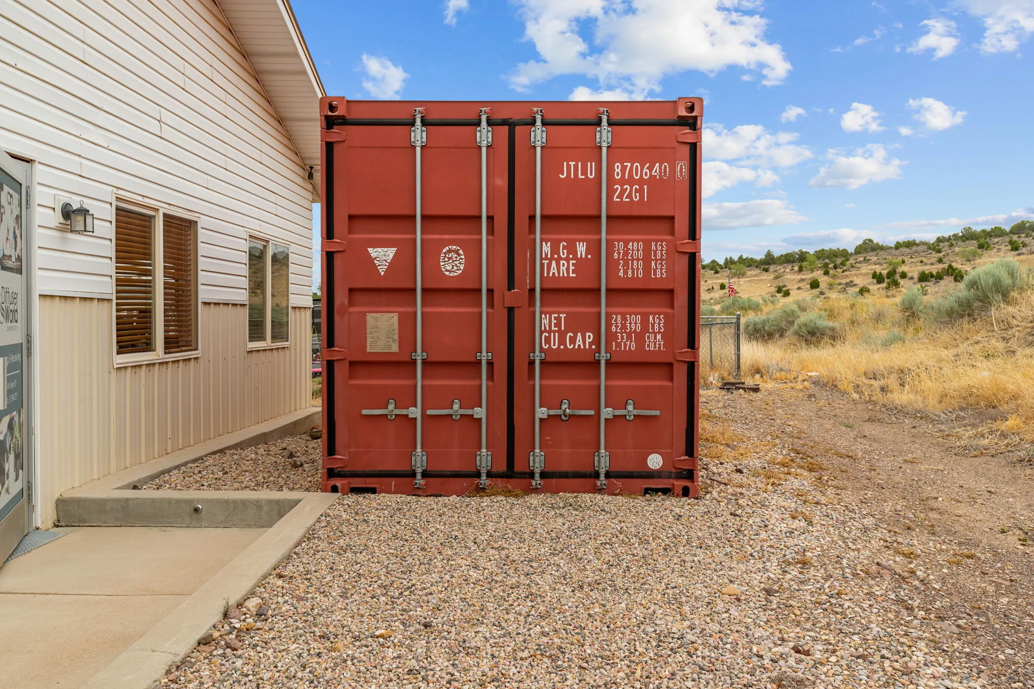 Exterior featuring a red shipping container on a gravel area, siding, and a concrete pathway
