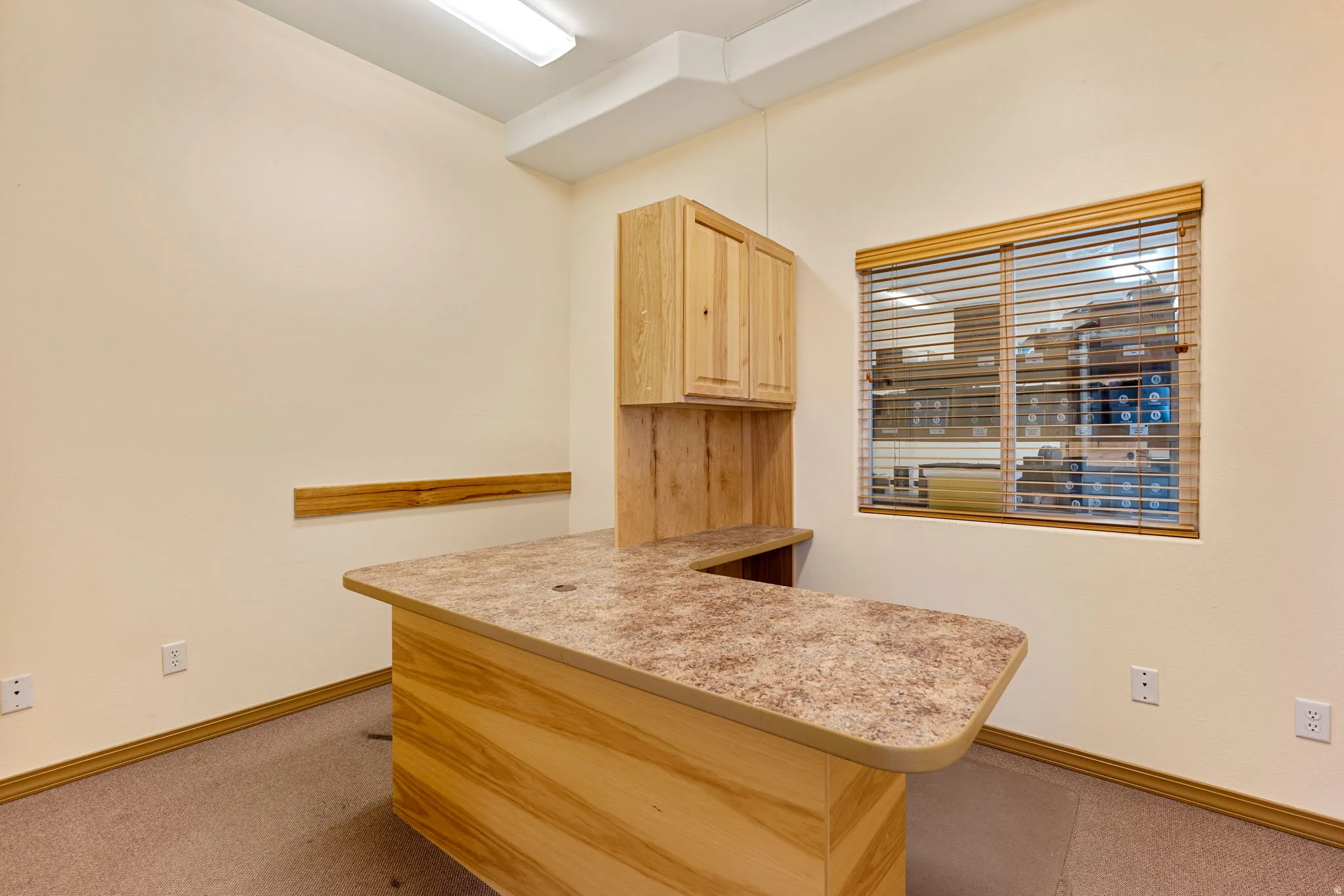 Dedicated workspace featuring a built-in U-shaped desk with a speckled countertop and light wood-finish cabinetry