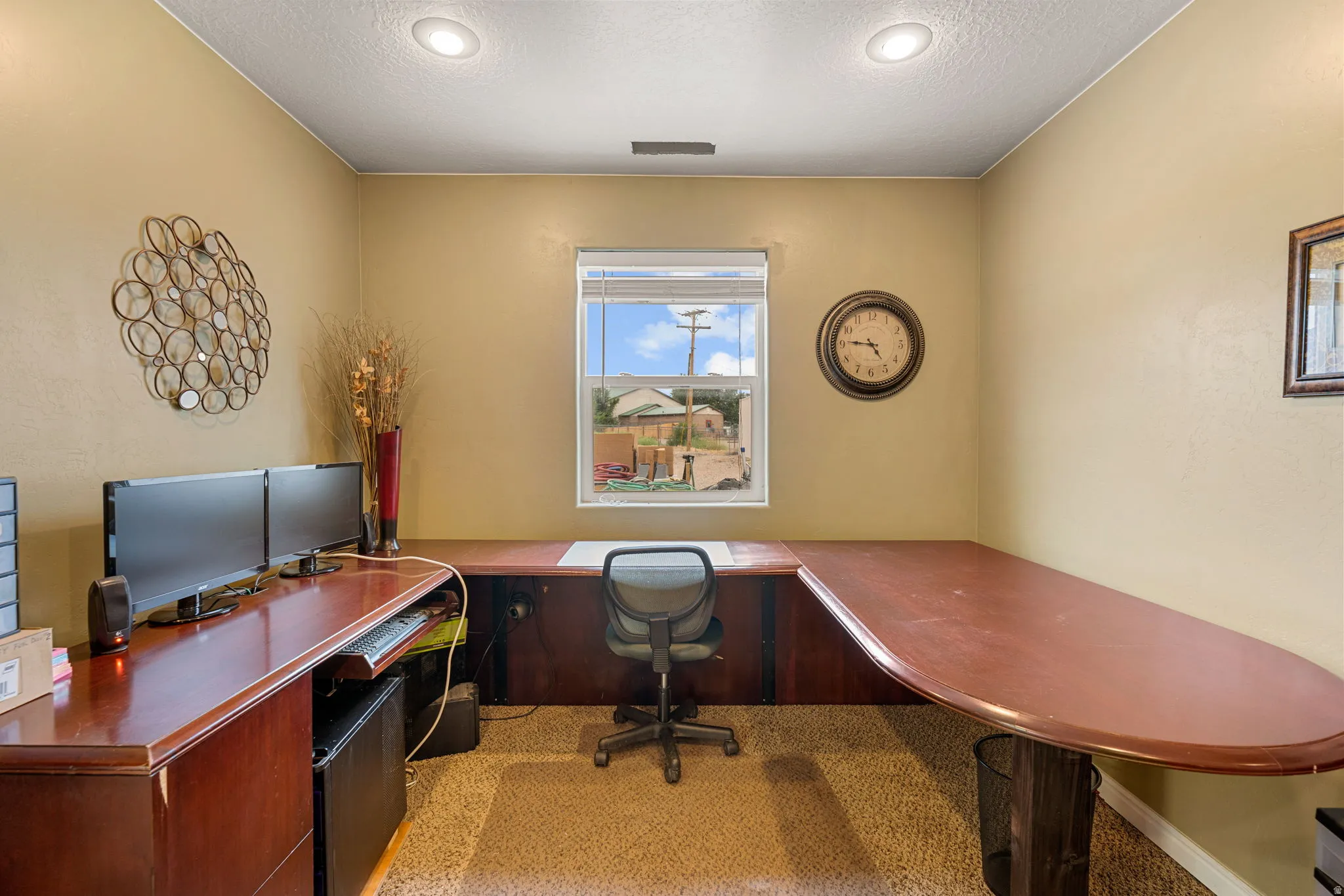 Built-in wrap-around desk with wood-finish surface, recessed ceiling lighting, single window, and neutral wall tones