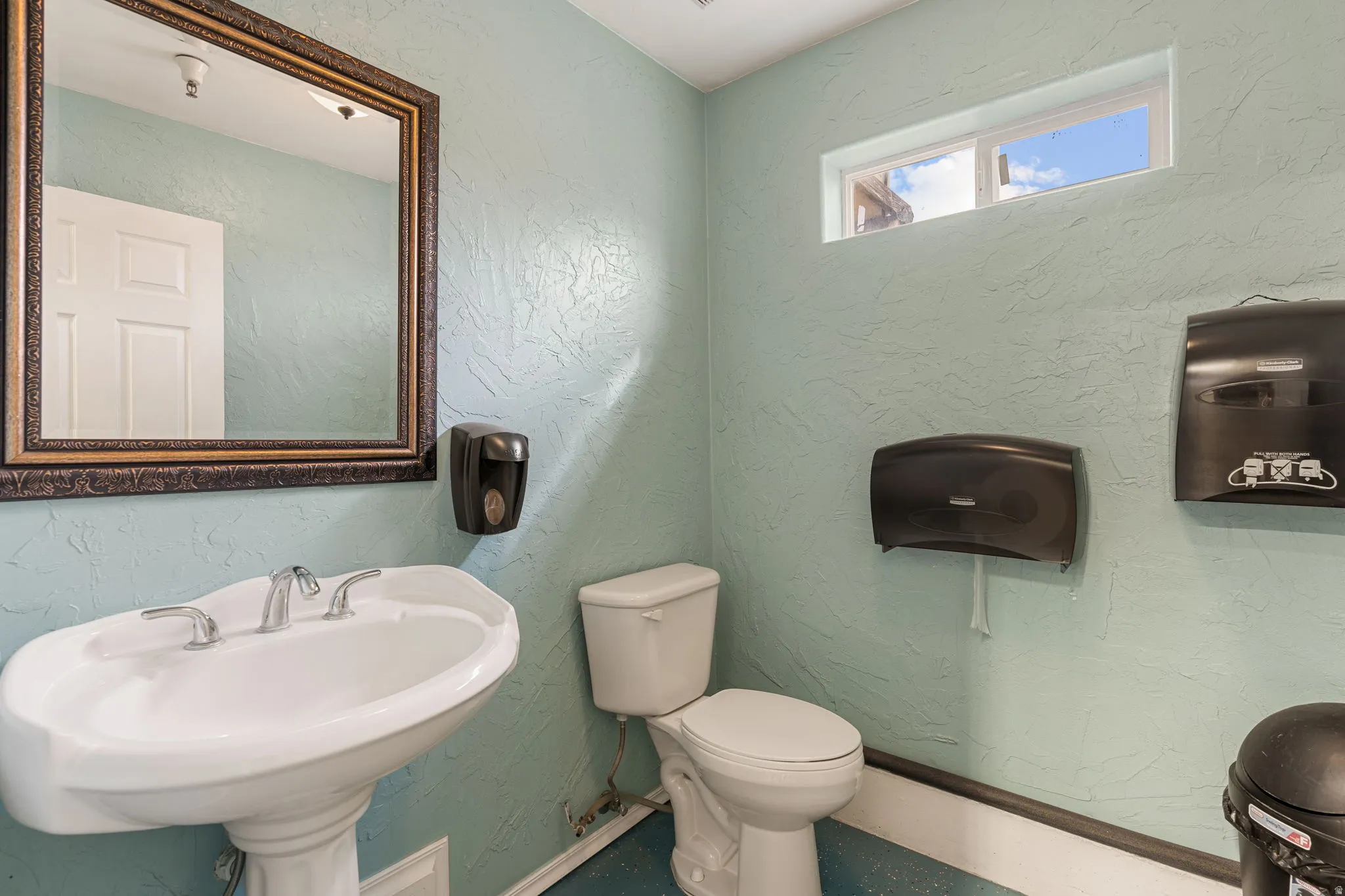 Pedestal sink with chrome fixtures and an ornate framed mirror