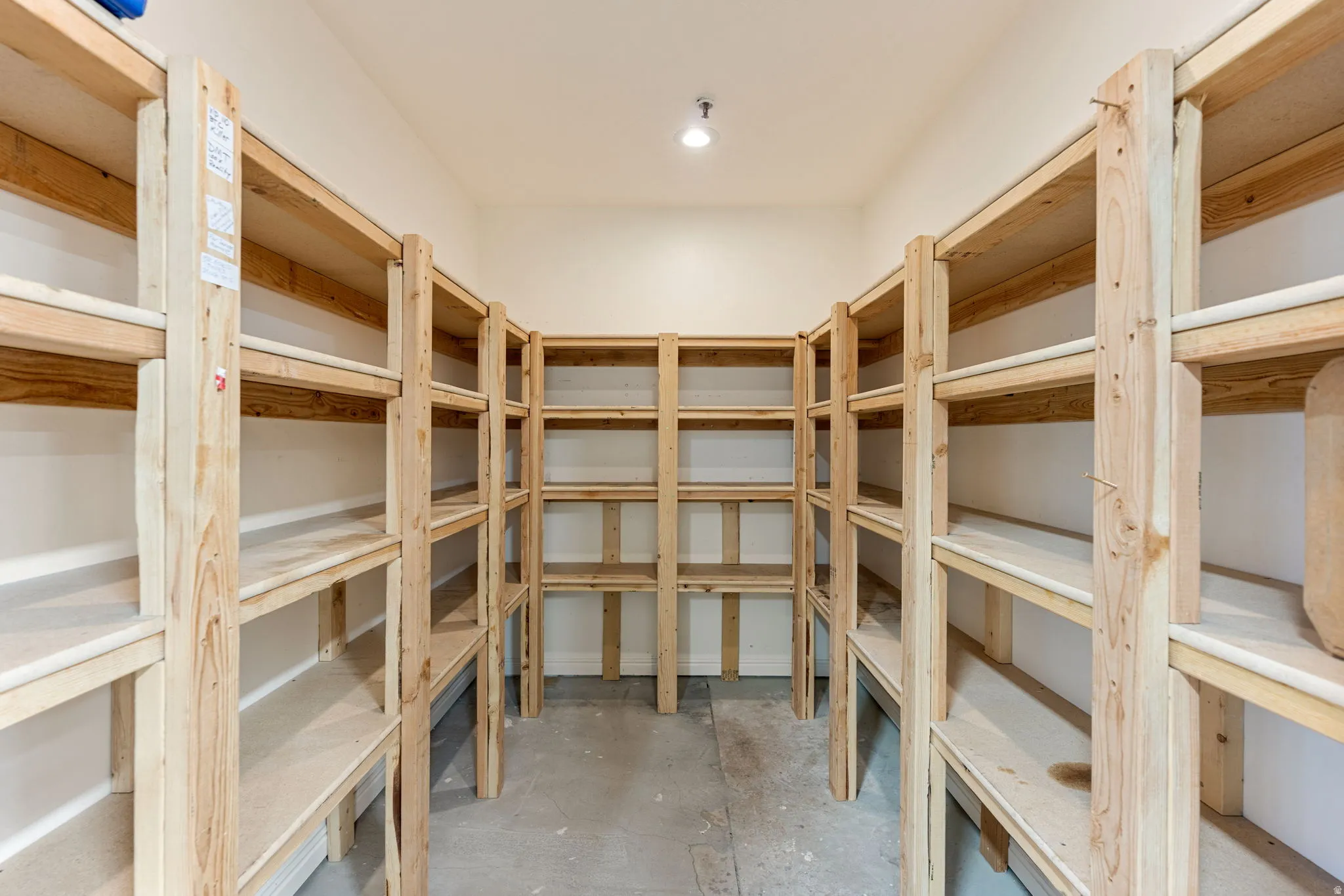Spacious storage room featuring extensive built-in wooden shelving, a light-colored concrete floor, and recessed ceiling lighting