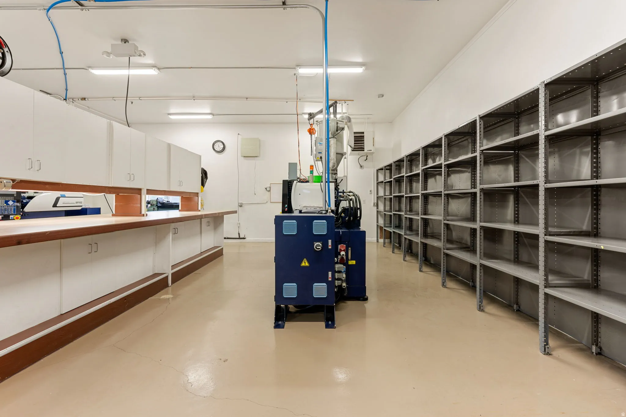 Utility room featuring extensive built-in cabinetry, durable flooring, multiple fluorescent lighting fixtures, and comprehensive wall-mounted shelving units
