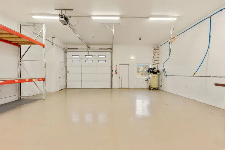 Spacious garage featuring a large overhead door with window inserts, high ceilings, multiple fluorescent light fixtures, and durable epoxy flooring