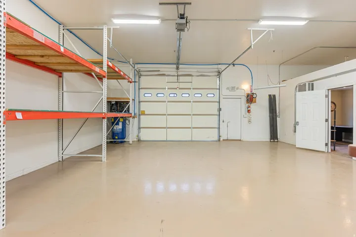 Spacious interior with an overhead garage door, industrial-style shelving, and light-toned flooring