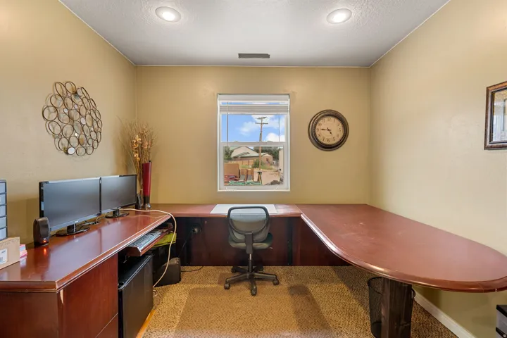 Built-in wrap-around desk with wood-finish surface, recessed ceiling lighting, single window, and neutral wall tones