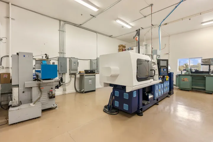 Spacious industrial interior featuring a large format machine, light-toned flooring, exposed conduit, white walls, and a window providing natural light
