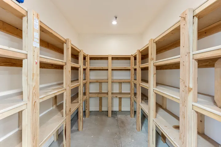 Spacious storage room featuring extensive built-in wooden shelving, a light-colored concrete floor, and recessed ceiling lighting