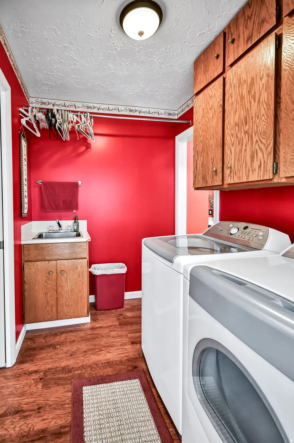 Dedicated laundry area featuring wood-finish flooring, overhead cabinetry, and a utility sink
