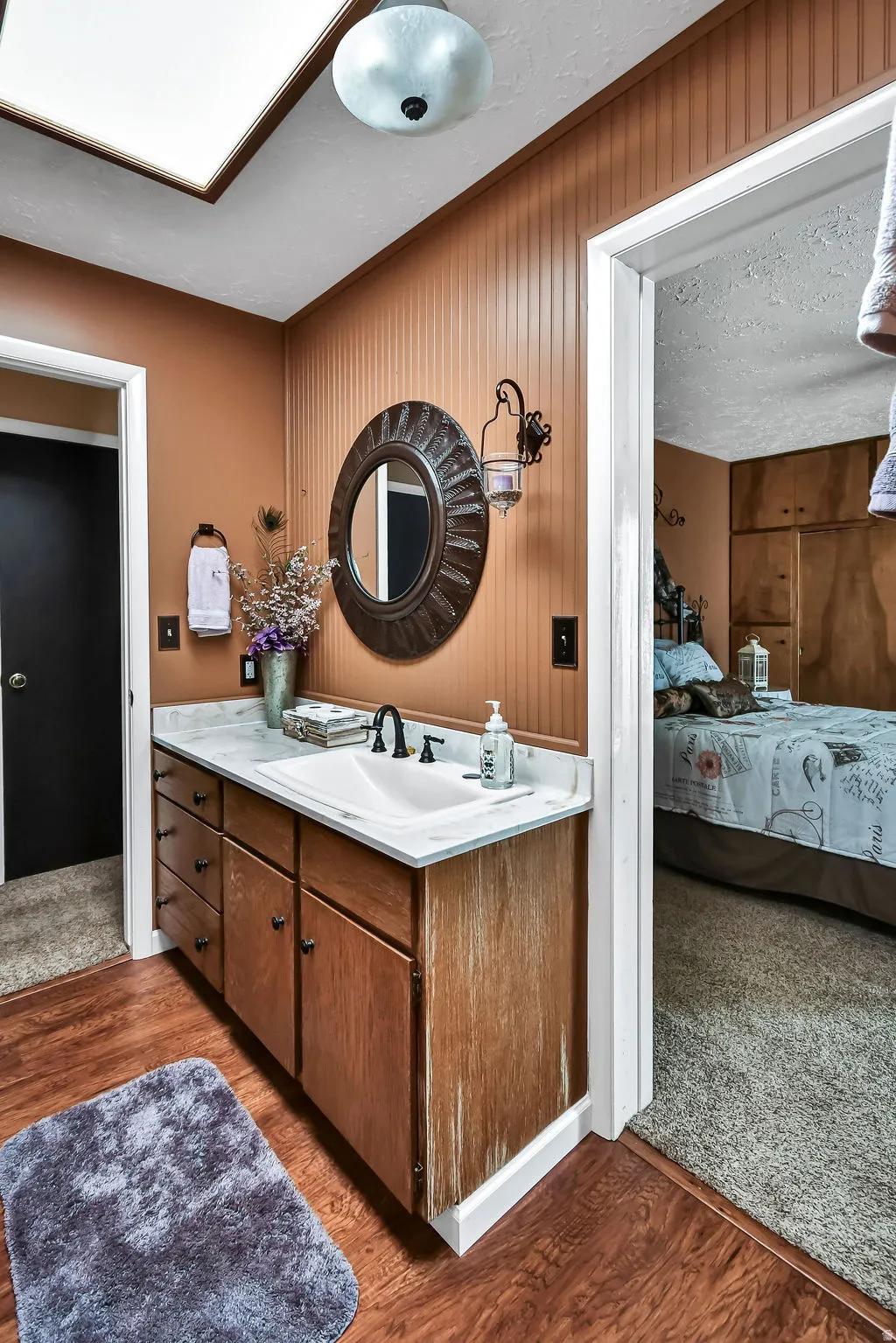Bathroom vanity with wood-finish cabinetry, a white countertop, and an undermount sink with a black faucet