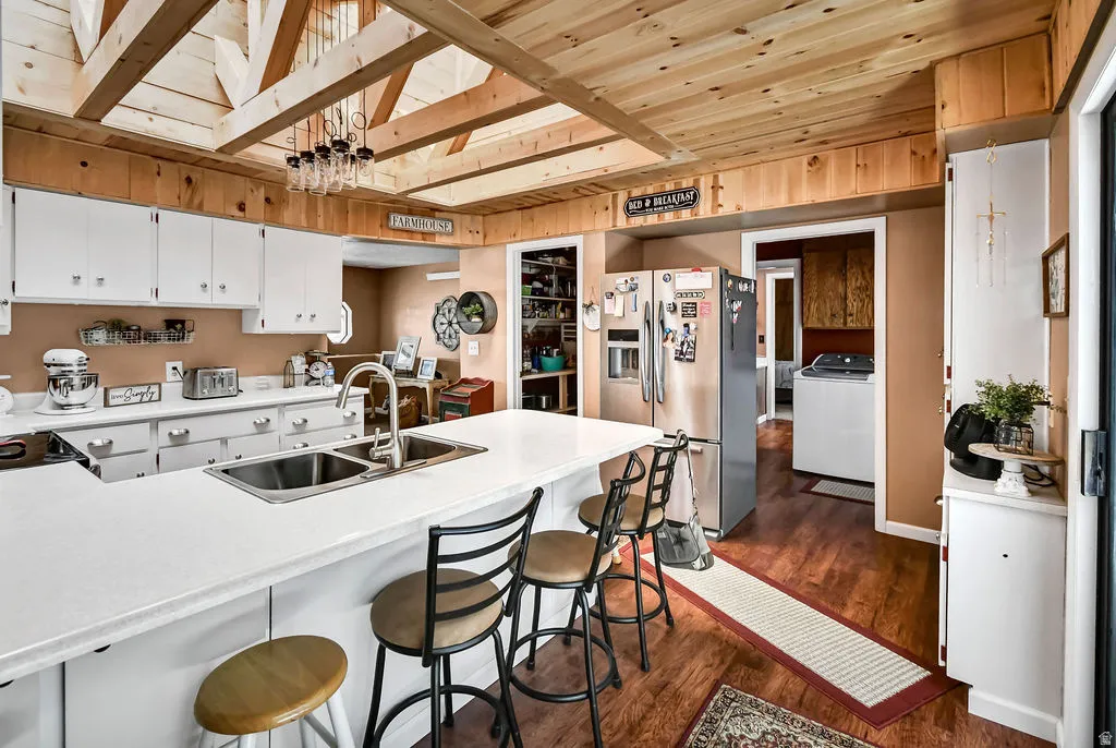 Kitchen with wood-finish flooring, exposed wood beam ceiling, white cabinetry, a double basin sink, and a counter-height island with seating