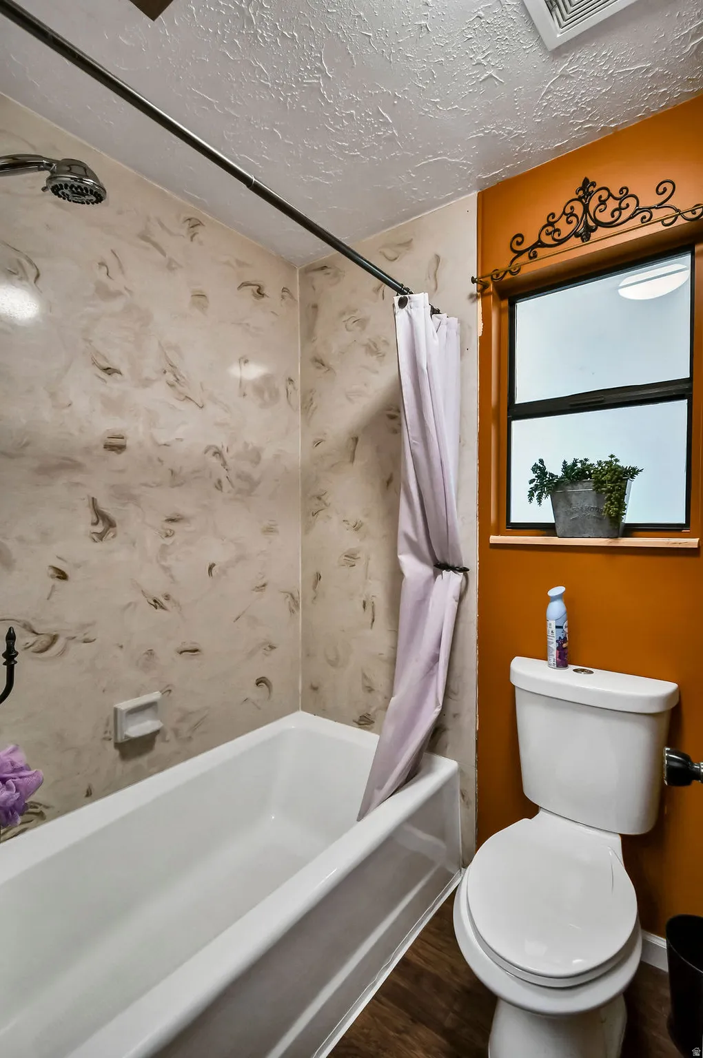 Full bathroom featuring a white bathtub and shower with patterned wall surround, a white toilet, and wood-finish flooring