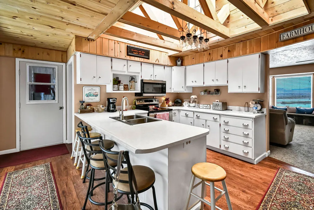 Kitchen featuring a large island with sink, white cabinetry, wood-finish flooring, and exposed timber ceiling beams