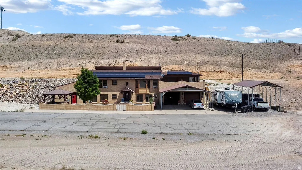 Multi-level property featuring a tan stucco exterior, solar panel arrays, and multiple covered parking structures