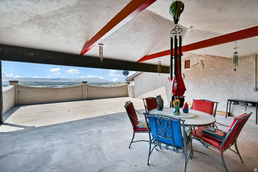 Expansive outdoor patio featuring a concrete floor, textured ceiling with exposed red beams, and a light-toned brick privacy wall