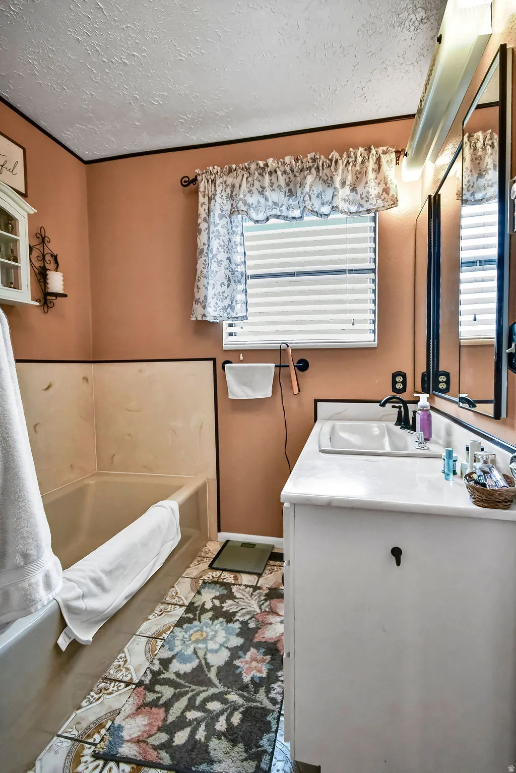 Bathroom featuring a white vanity with integrated sink, dual mirrors with overhead lighting, a bathtub with shower surround, and a window with blinds