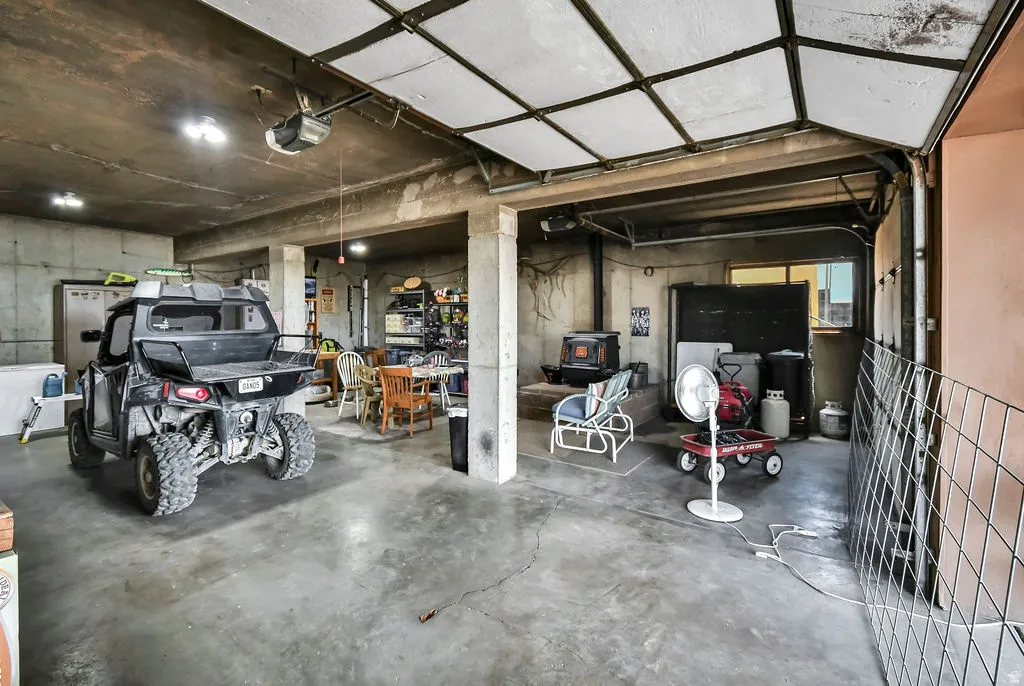 Concrete floor garage featuring a wood-burning stove, exposed concrete walls, and overhead lighting