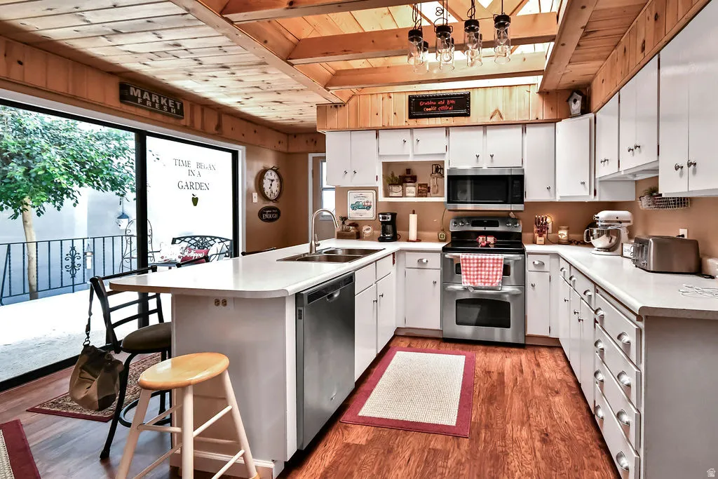 U-shaped kitchen featuring white cabinetry, light countertops, wood-finish flooring, and stainless steel appliances