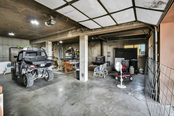 Concrete floor garage featuring a wood-burning stove, exposed concrete walls, and overhead lighting