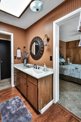 Bathroom vanity with wood-finish cabinetry, a white countertop, and an undermount sink with a black faucet