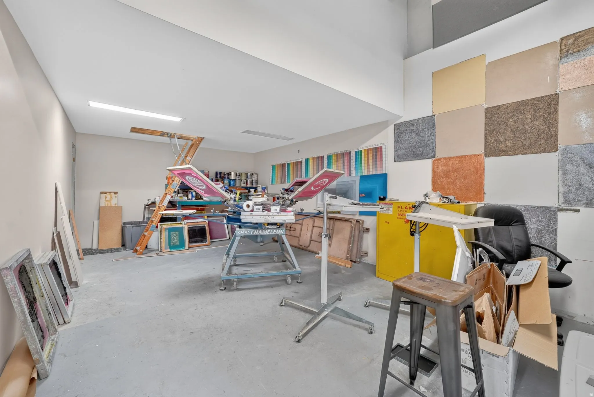 Spacious workroom featuring high ceilings with integrated fluorescent lighting, concrete flooring, and a dedicated workspace