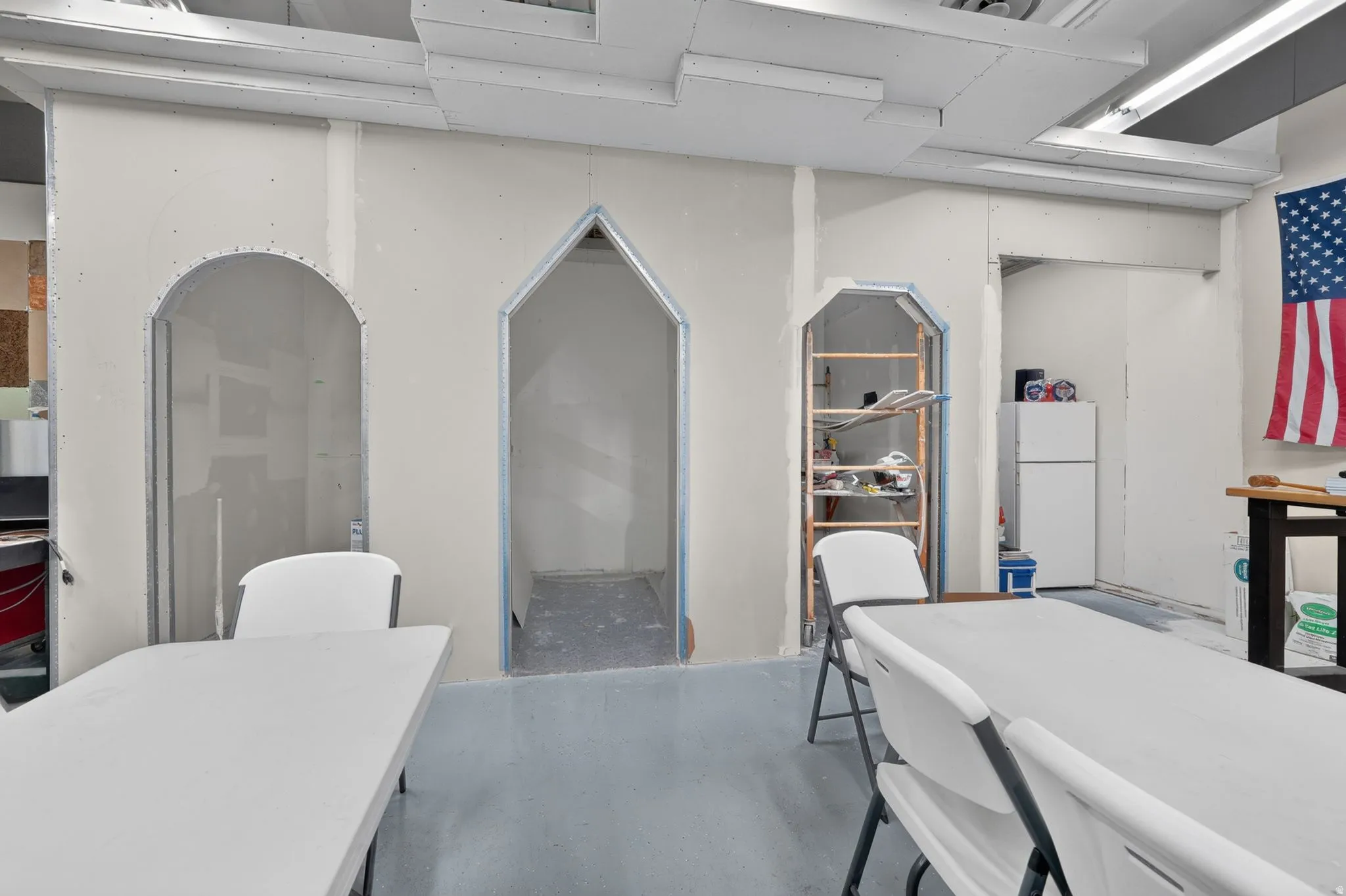 Unfinished interior space featuring multiple arched openings, exposed metal framing, and a dropped ceiling grid