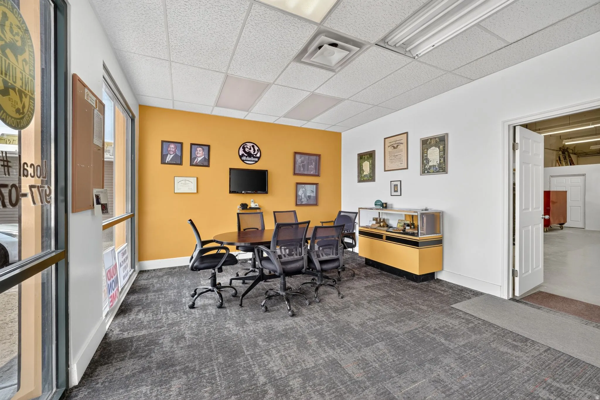Office space featuring a vibrant accent wall, expansive window frontage, suspended ceiling, and low-pile carpet flooring