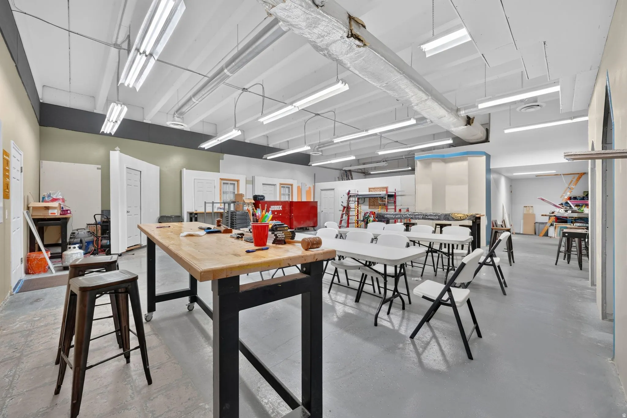 Spacious interior featuring high ceilings, exposed ductwork, and fluorescent lighting