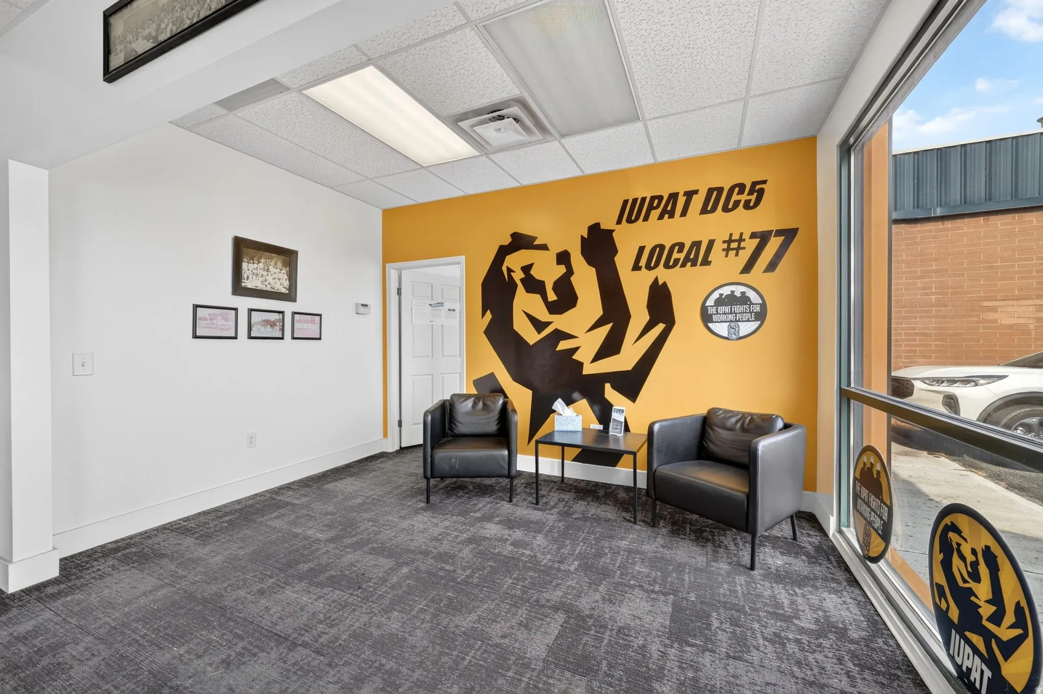 Entryway featuring a large picture window, commercial-grade carpet flooring, drop ceiling with fluorescent lighting, and a white paneled door