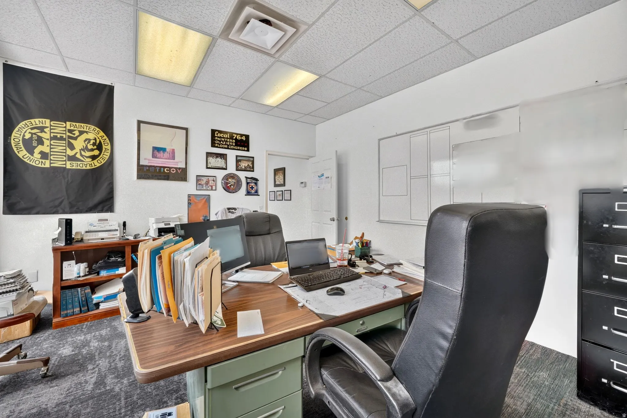 Office space with white walls, textured gray carpet, and a white acoustical tile ceiling with recessed lighting