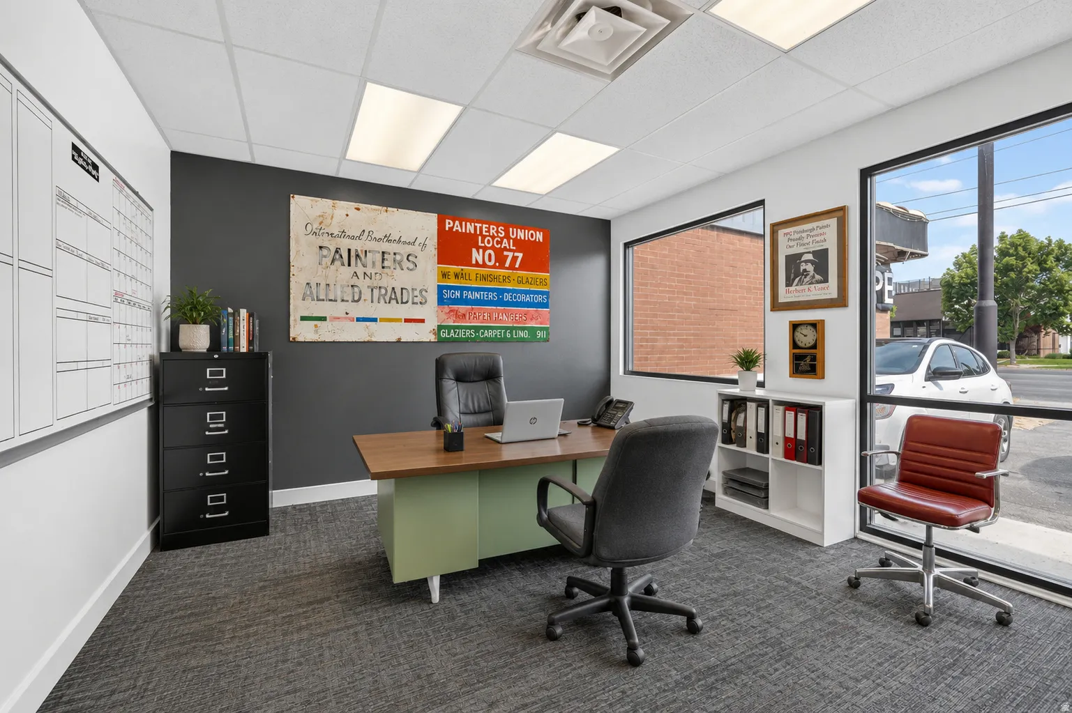 Office space featuring large storefront windows, dropped ceiling with integrated lighting, dark gray accent wall, and textured gray carpeting