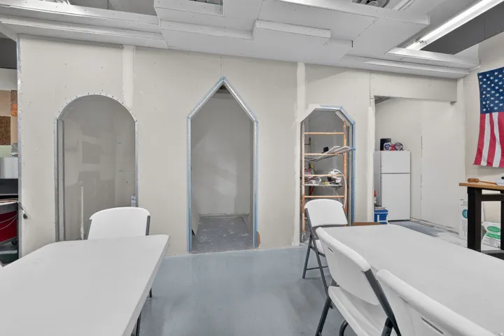 Unfinished interior space featuring multiple arched openings, exposed metal framing, and a dropped ceiling grid