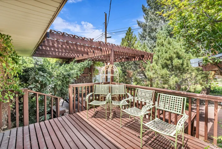 Spacious wood deck featuring a slatted pergola, wood railing, and surrounding mature foliage