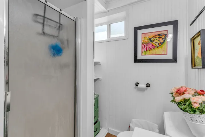 Frosted glass shower enclosure, white beadboard wall paneling, small transom window, built-in shelving, and a toilet