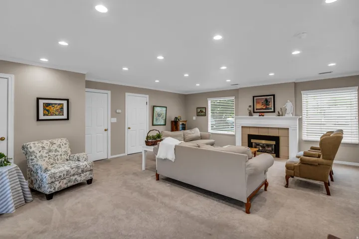 Spacious living area featuring neutral carpeting, recessed lighting, and a prominent fireplace with a white mantel and tile surround