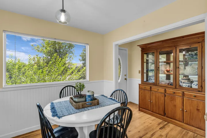 Dining area featuring a wide window with blinds, wood-finish flooring, and white wainscoting