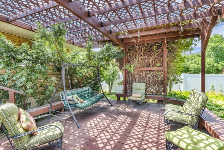 Spacious wooden deck featuring a lattice-style pergola, string lighting, built-in wooden benches, and established greenery