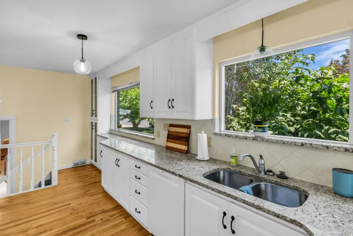 Kitchen featuring wood-finish flooring, white cabinetry, a dual basin stainless steel sink, and light-toned countertops