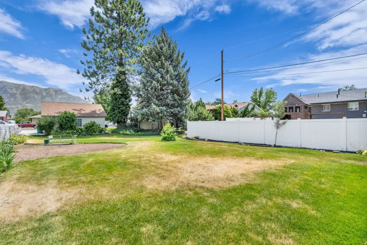 Expansive grass area featuring mature trees and a white privacy fence